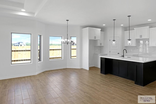 kitchen featuring sink, a center island with sink, an inviting chandelier, light hardwood / wood-style floors, and white cabinetry