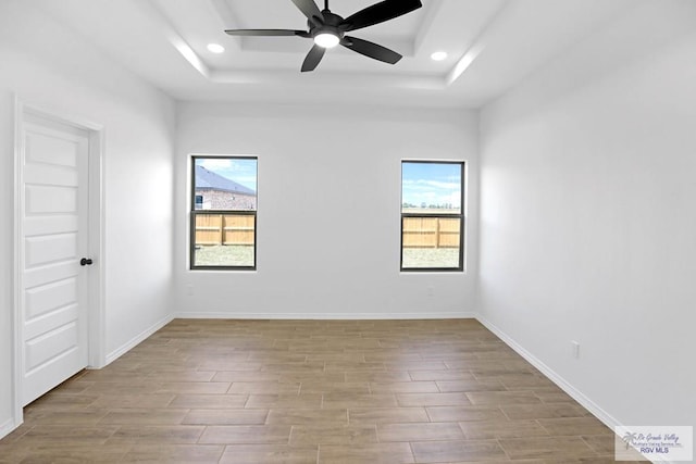 spare room featuring ceiling fan, light hardwood / wood-style flooring, and a tray ceiling