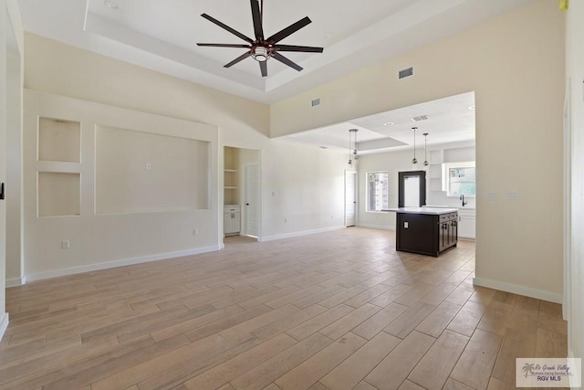 32773 Jorge St, Los Fresnos, TX 78566 - unfurnished living room with a ceiling fan, light wood-type flooring, a raised ceiling, baseboards, and visible vents