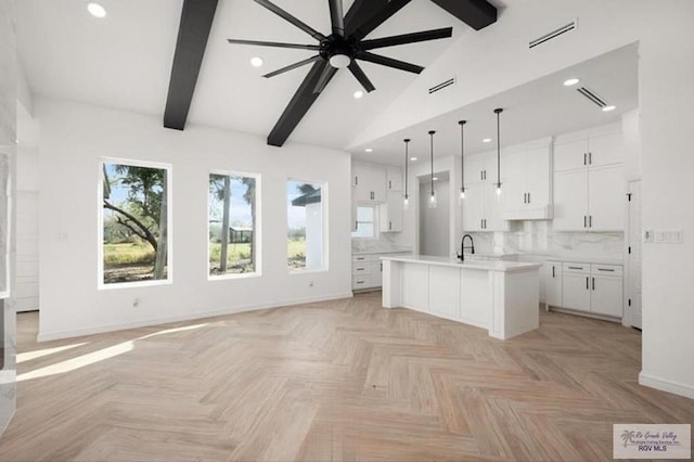 kitchen featuring light countertops, tasteful backsplash, a center island with sink, and white cabinetry