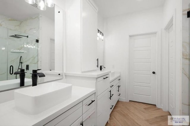 full bath featuring two vanities, a sink, and a marble finish shower