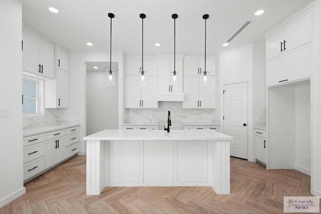 kitchen with visible vents, hanging light fixtures, a kitchen island with sink, light countertops, and white cabinetry