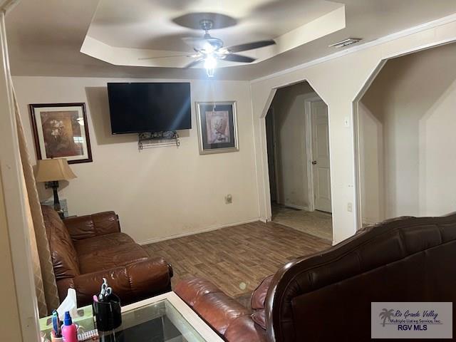 living room with hardwood / wood-style flooring, ceiling fan, and a raised ceiling