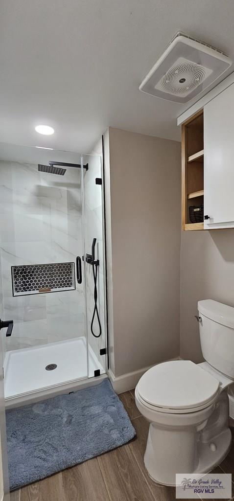 bathroom with hardwood / wood-style floors, toilet, and an enclosed shower