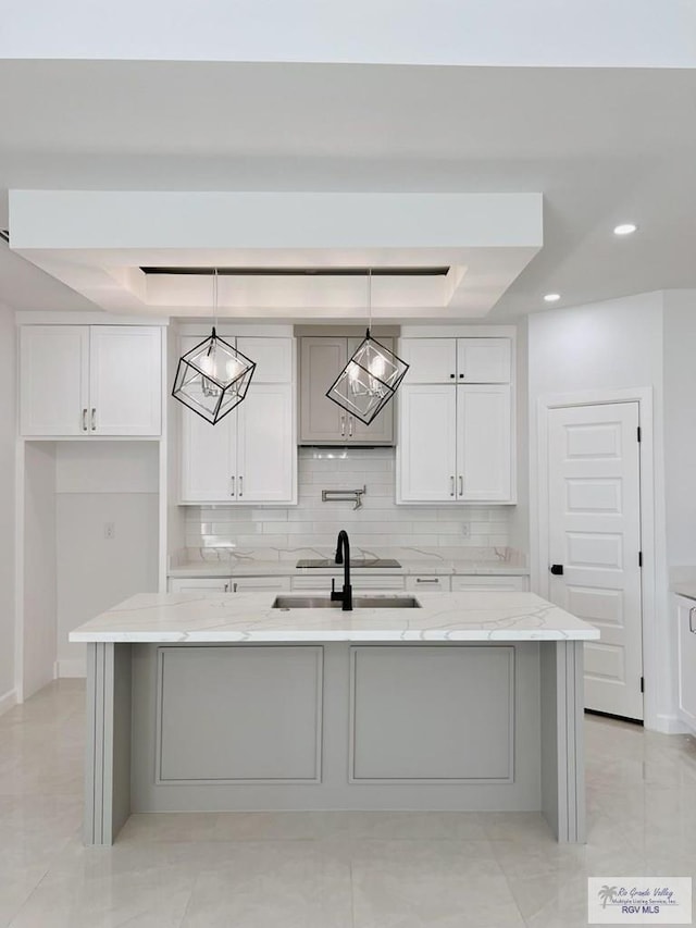 kitchen with white cabinetry, light stone countertops, a center island with sink, and decorative light fixtures