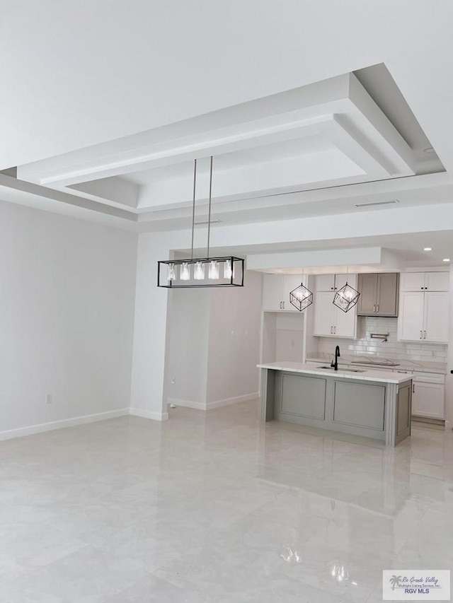 kitchen with pendant lighting, sink, a kitchen island with sink, backsplash, and a raised ceiling