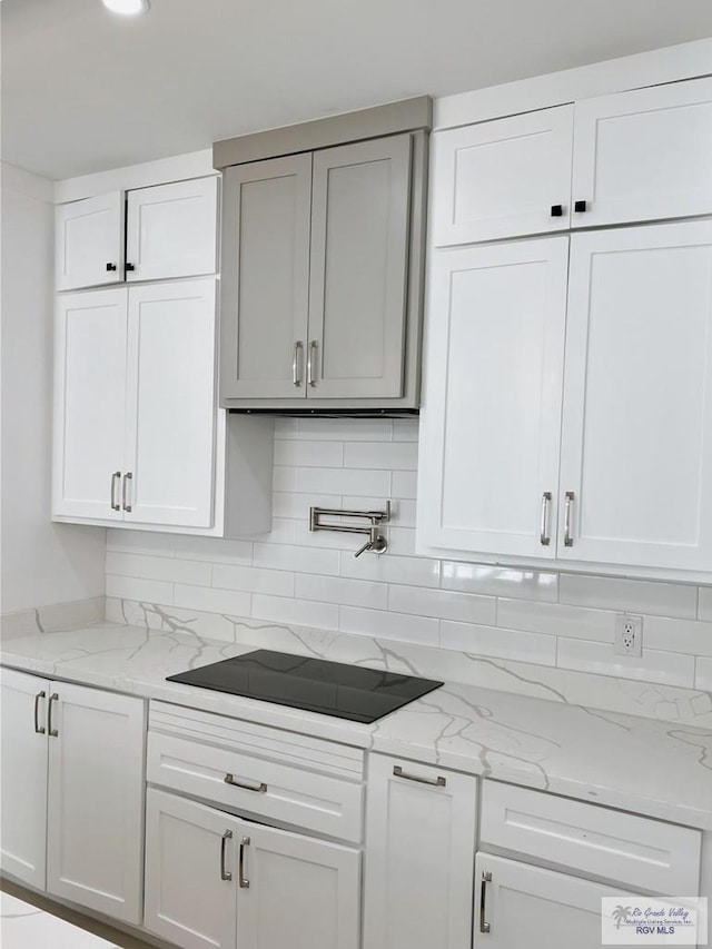 kitchen featuring tasteful backsplash, white cabinetry, black electric stovetop, and light stone counters