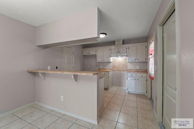 kitchen featuring light tile patterned floors, a kitchen breakfast bar, a textured ceiling, white cabinets, and kitchen peninsula