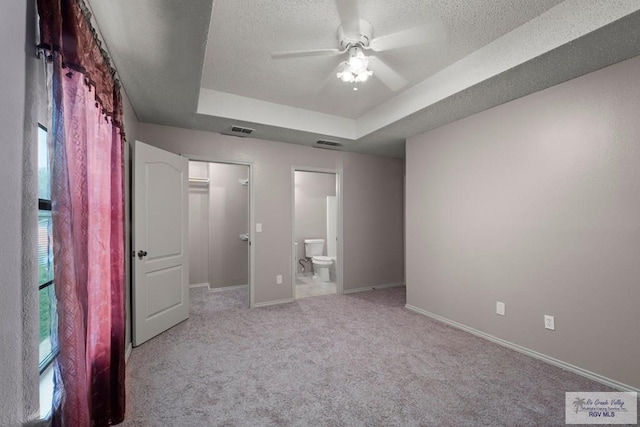 unfurnished bedroom with a walk in closet, a raised ceiling, light carpet, and a textured ceiling