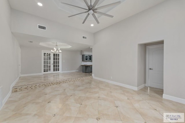 unfurnished living room featuring ceiling fan with notable chandelier and a tray ceiling