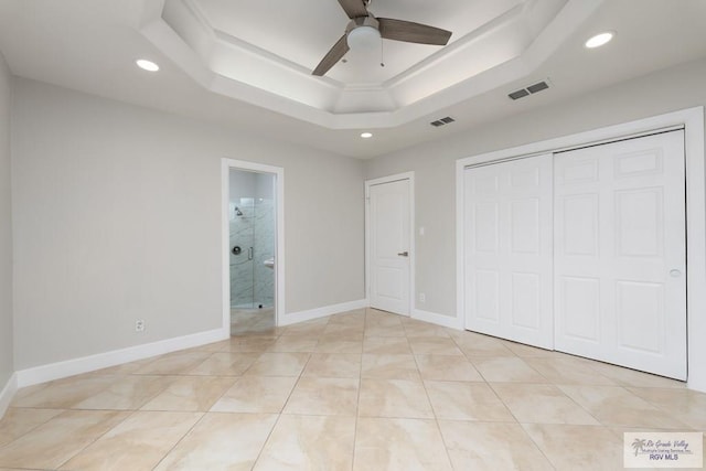 unfurnished bedroom featuring ceiling fan, light tile patterned flooring, a raised ceiling, and ensuite bath