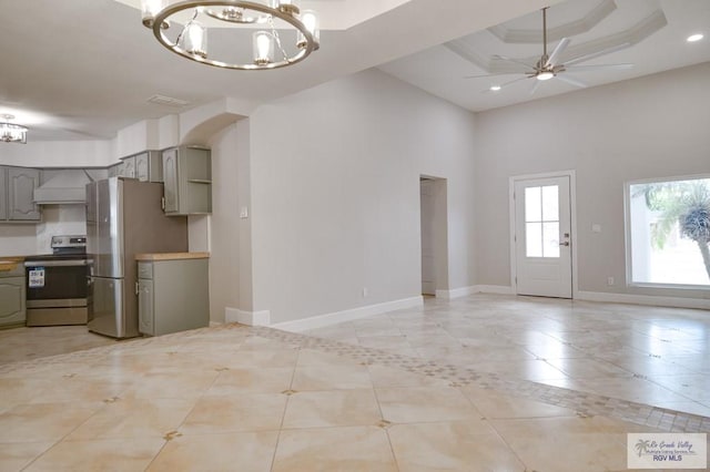 kitchen with gray cabinetry, ceiling fan with notable chandelier, a raised ceiling, appliances with stainless steel finishes, and custom range hood