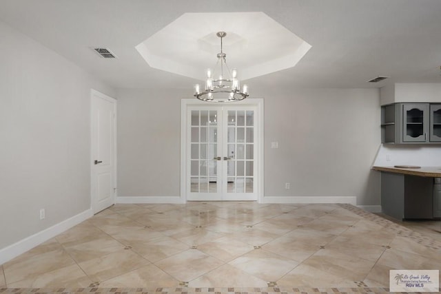 unfurnished dining area featuring a notable chandelier, french doors, and a tray ceiling