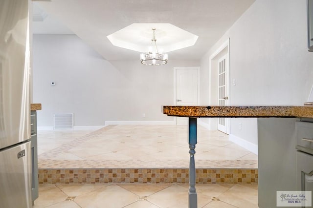 kitchen featuring white cabinets, a tray ceiling, pendant lighting, a chandelier, and stainless steel refrigerator