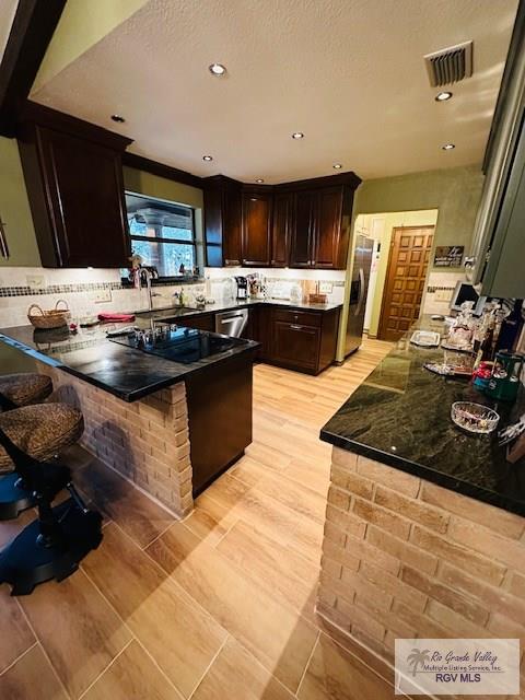 kitchen with sink, a kitchen bar, kitchen peninsula, stainless steel appliances, and dark brown cabinets