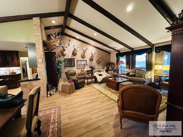 living room with ornate columns, brick wall, light hardwood / wood-style flooring, and vaulted ceiling with beams