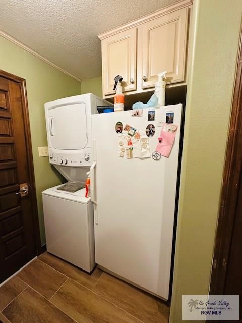 clothes washing area featuring cabinets, stacked washing maching and dryer, and a textured ceiling