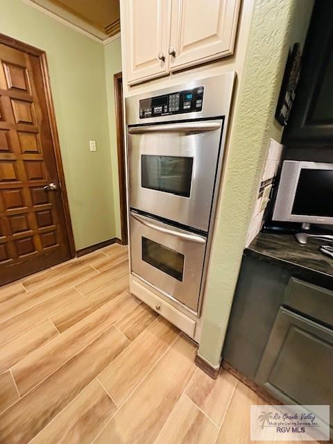 kitchen featuring white cabinetry, stainless steel double oven, and crown molding