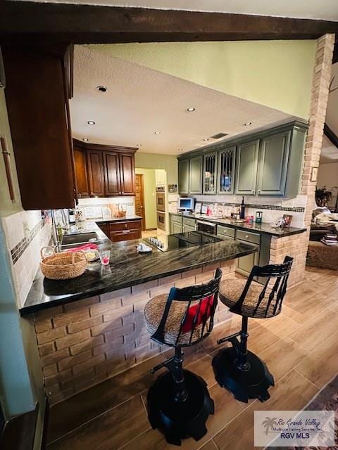 kitchen featuring a breakfast bar, sink, black electric stovetop, green cabinets, and kitchen peninsula