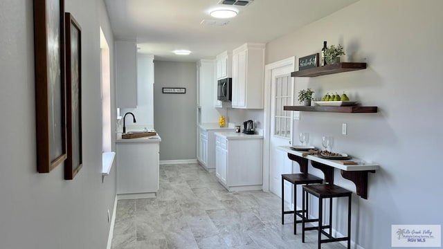 902 Rio Hondo Rd, Harlingen, TX 78550 - kitchen featuring white cabinetry, a sink, baseboards, light marble finish flooring, and light countertops