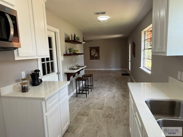902 Rio Hondo Rd, Harlingen, TX 78550 - kitchen with stainless steel microwave, white cabinets, open shelves, baseboards, and a sink