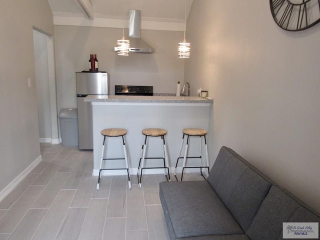 kitchen featuring pendant lighting, wall chimney exhaust hood, a breakfast bar, and stainless steel refrigerator