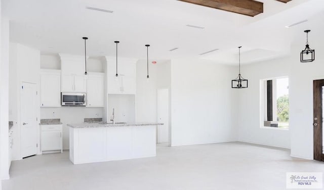 33521 Stanford Rd, Los Fresnos, TX 78566 - kitchen with stainless steel microwave, a sink, white cabinetry, pendant lighting, and a center island with sink