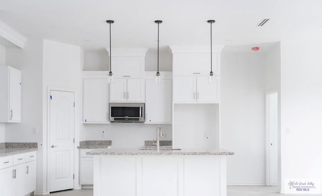 33521 Stanford Rd, Los Fresnos, TX 78566 - kitchen featuring stainless steel microwave, a sink, a kitchen island, white cabinetry, and decorative light fixtures