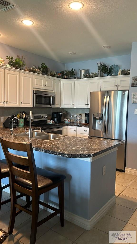 kitchen featuring light tile patterned flooring, white cabinets, stainless steel appliances, and a textured ceiling