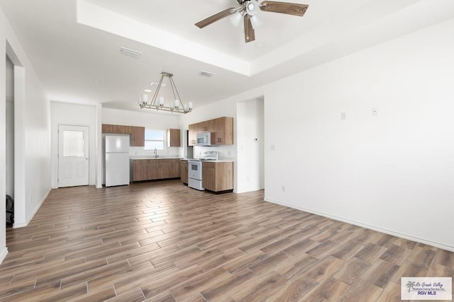 kitchen featuring hardwood / wood-style floors, white appliances, ceiling fan with notable chandelier, a tray ceiling, and decorative light fixtures