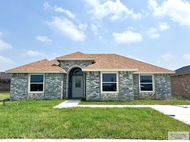 view of front facade with brick siding, a front yard, and roof with shingles