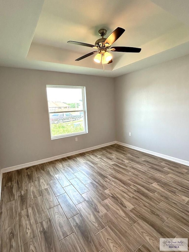 empty room with baseboards, a raised ceiling, and dark wood-style floors