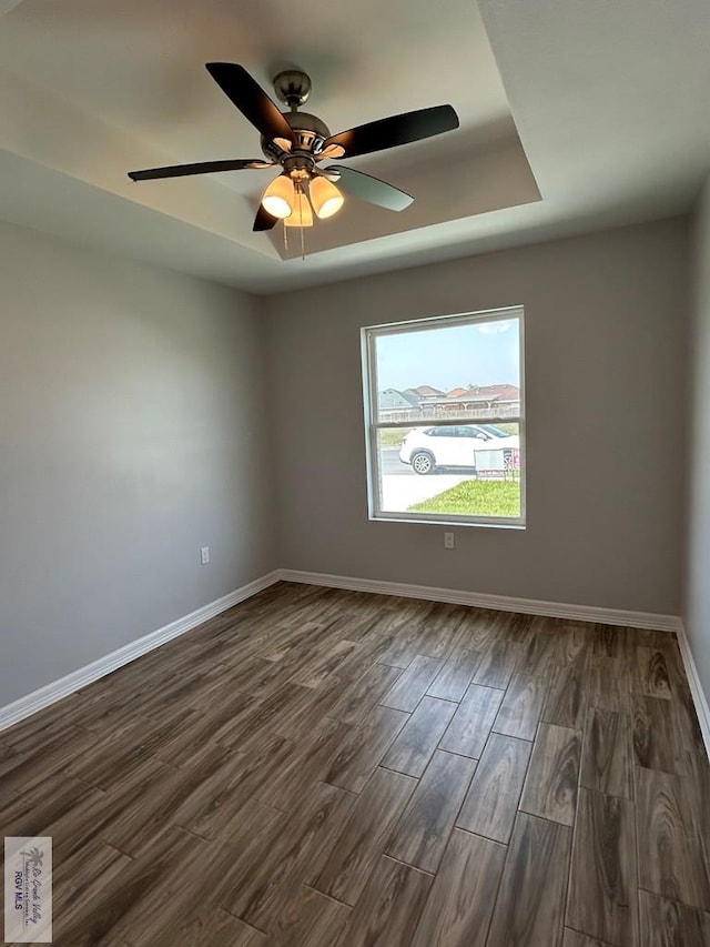 unfurnished room with dark wood finished floors, ceiling fan, baseboards, and a tray ceiling