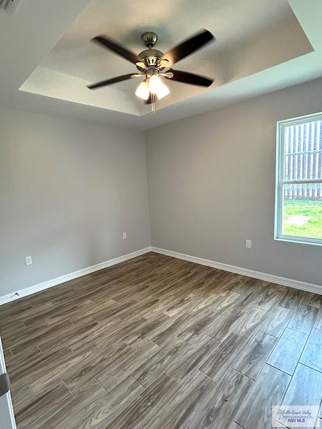 empty room featuring a raised ceiling, baseboards, dark wood-style flooring, and ceiling fan