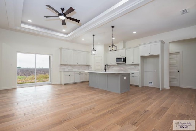 kitchen with white cabinetry, hanging light fixtures, a raised ceiling, and an island with sink