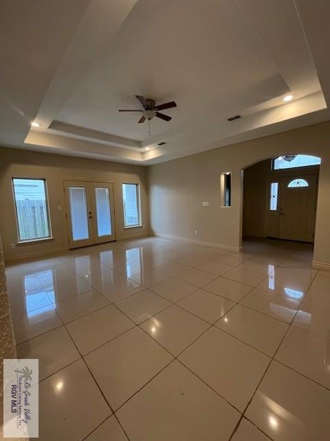 empty room with a raised ceiling, ceiling fan, and light tile patterned flooring