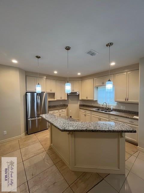 kitchen with a center island, stainless steel fridge, sink, and hanging light fixtures