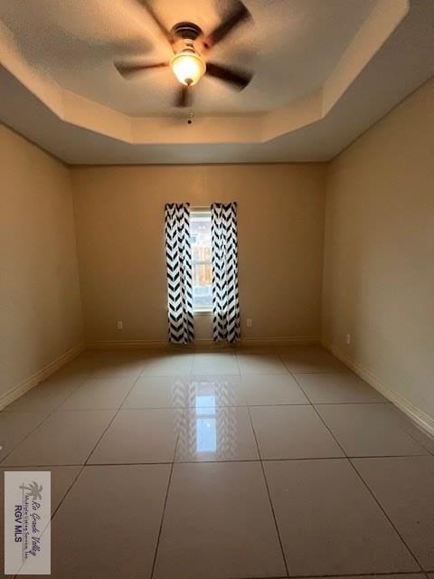 unfurnished room featuring light tile patterned floors, a tray ceiling, and ceiling fan