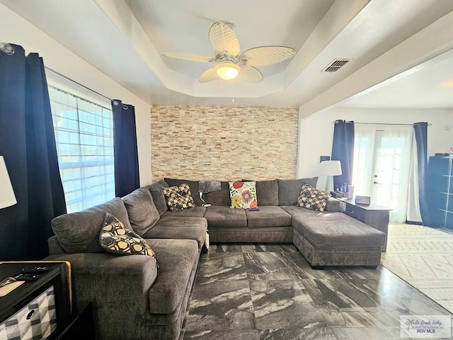 living room featuring a raised ceiling, a wealth of natural light, and ceiling fan