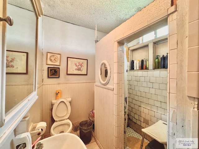 bathroom with wood walls, a shower, toilet, a textured ceiling, and tile walls