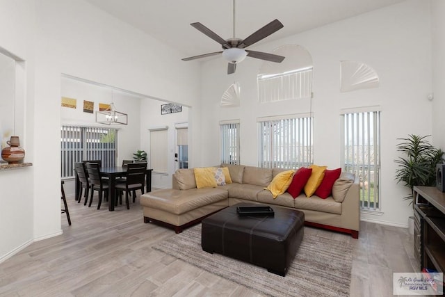 living room with a towering ceiling, baseboards, wood finished floors, and ceiling fan with notable chandelier