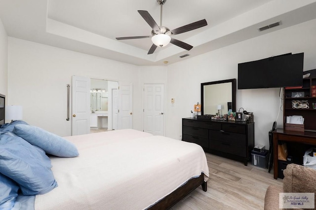 bedroom with ceiling fan, a tray ceiling, light wood-style flooring, and visible vents