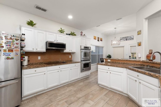 kitchen with light wood-style flooring, a sink, white cabinets, appliances with stainless steel finishes, and tasteful backsplash