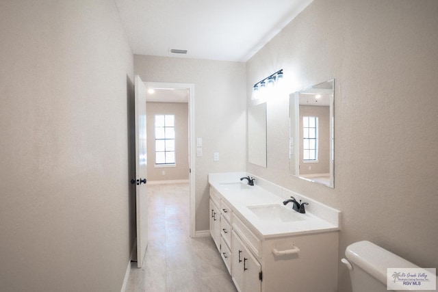 23919 Ellie Ln, Harlingen, TX 78552 - bathroom featuring toilet, double vanity, plenty of natural light, and baseboards