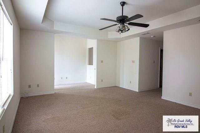 empty room featuring light carpet, ceiling fan, and a tray ceiling