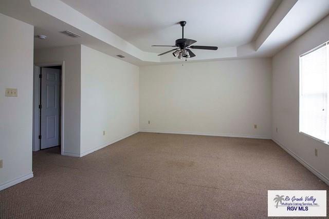 unfurnished room featuring ceiling fan, a tray ceiling, and carpet