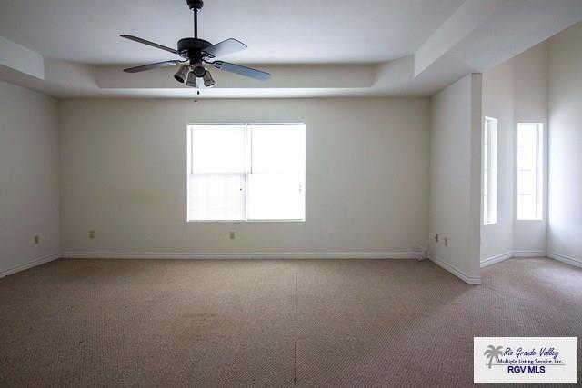 carpeted empty room featuring ceiling fan and a tray ceiling