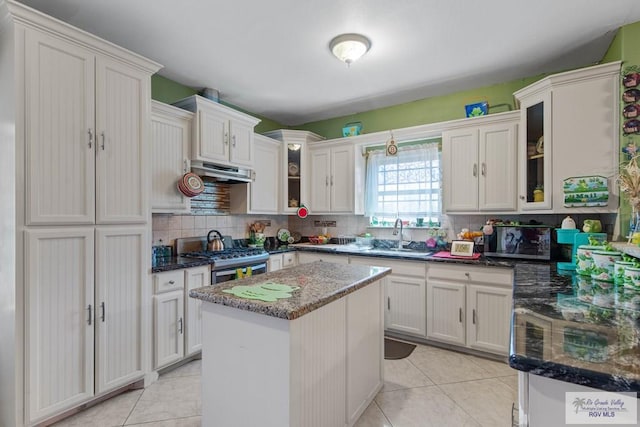 kitchen featuring sink, backsplash, dark stone counters, a center island, and stainless steel gas range oven