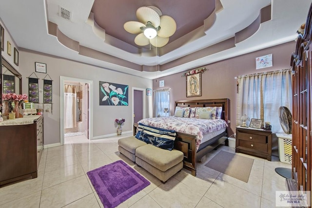 bedroom featuring ensuite bath, light tile patterned floors, ceiling fan, and a tray ceiling