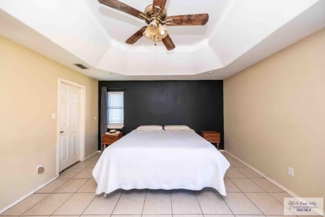 bedroom featuring light tile patterned floors, a tray ceiling, visible vents, and baseboards